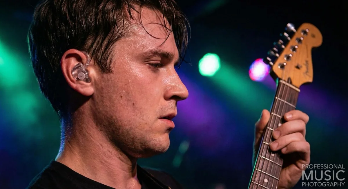 Musician guitarist wearing transparent custom musicians earplugs during live concert performance